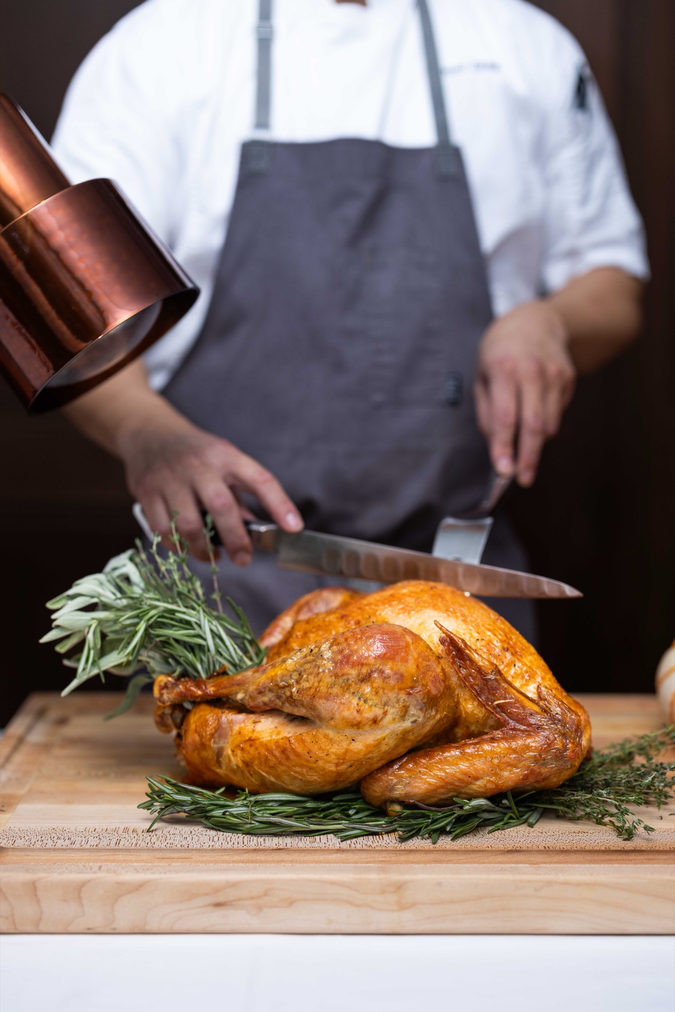 Chef carving a roast turkey under a copper heat lamp at the carving station