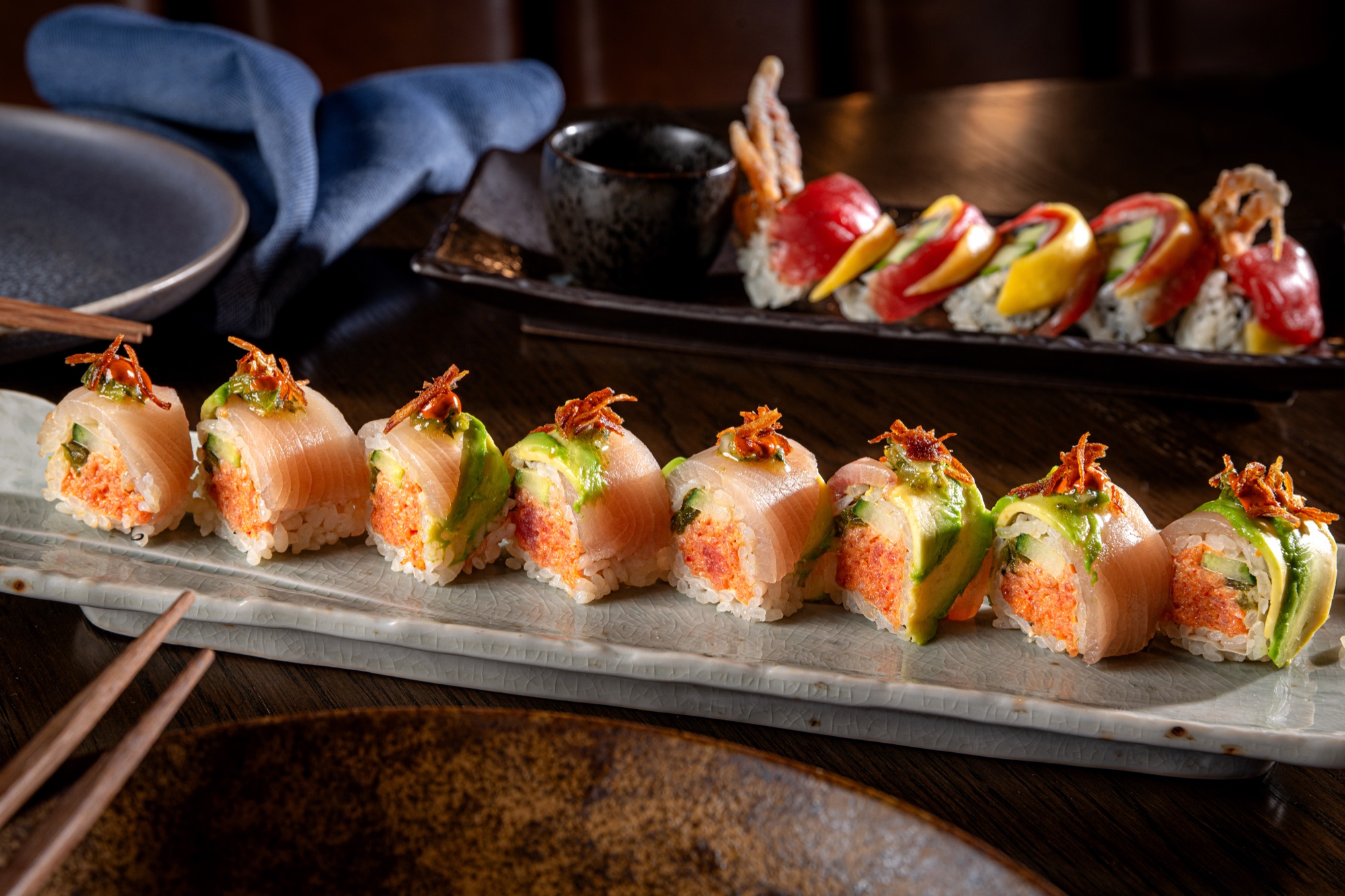 Signature sushi rolls topped with crispy garnish on a long stone plate